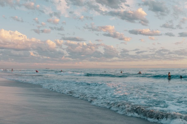 anonymous travelers swimming in wavy ocean at sundown