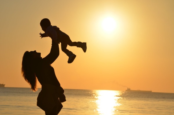 woman carrying baby at beach during sunset